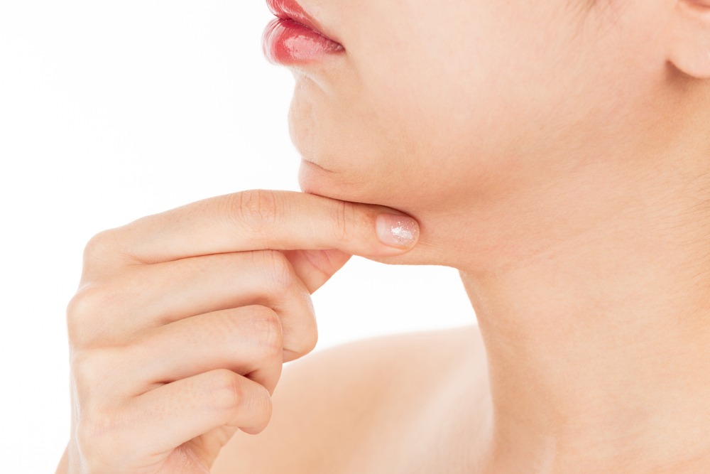 Close-up of a woman's chin and jawline, highlighting skincare and beauty routines. The woman gently touches her chin with her fingers, emphasizing self-care and facial aesthetics against a plain white background.
