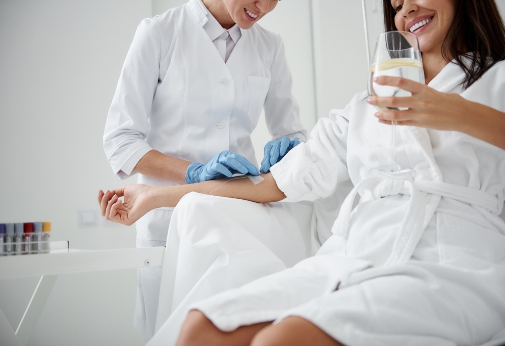 woman in white bathrobe receives IV vitamin therapy from clinician