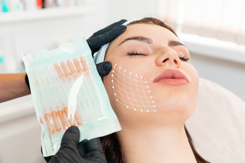 Aesthetic treatment session in a clinic, featuring a woman receiving facial injections. The practitioner holds a pack of syringes, indicating a cosmetic procedure aimed at enhancing facial contours and rejuvenation.