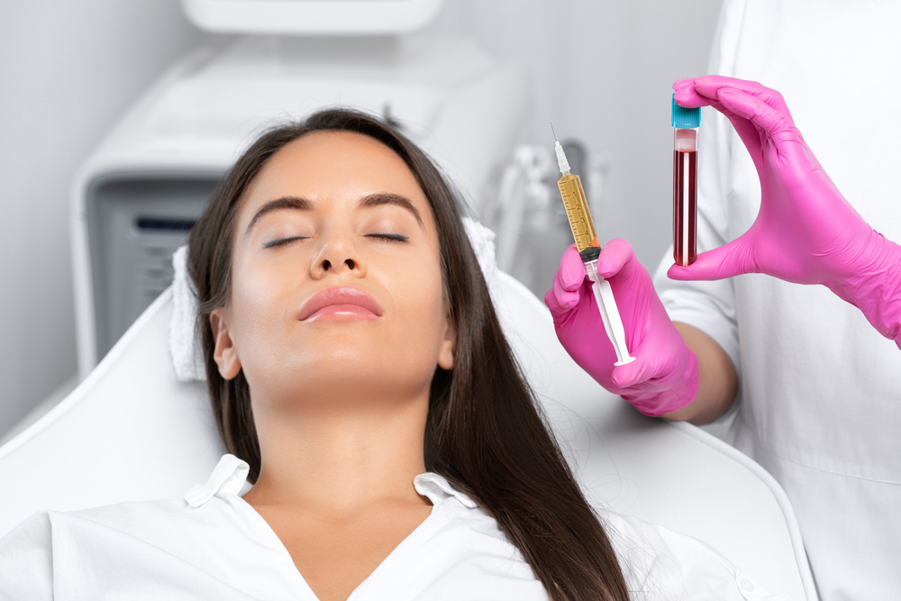 Woman receiving a cosmetic treatment in a clinic, with a healthcare professional holding a syringe and a vial of blood, highlighting the use of blood-derived products in aesthetic procedures.