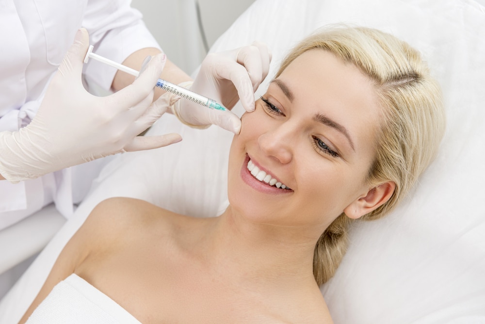 Aesthetic treatment session showing a smiling woman receiving an injectable cosmetic procedure from a practitioner, highlighting the growing popularity of non-surgical facial enhancements.