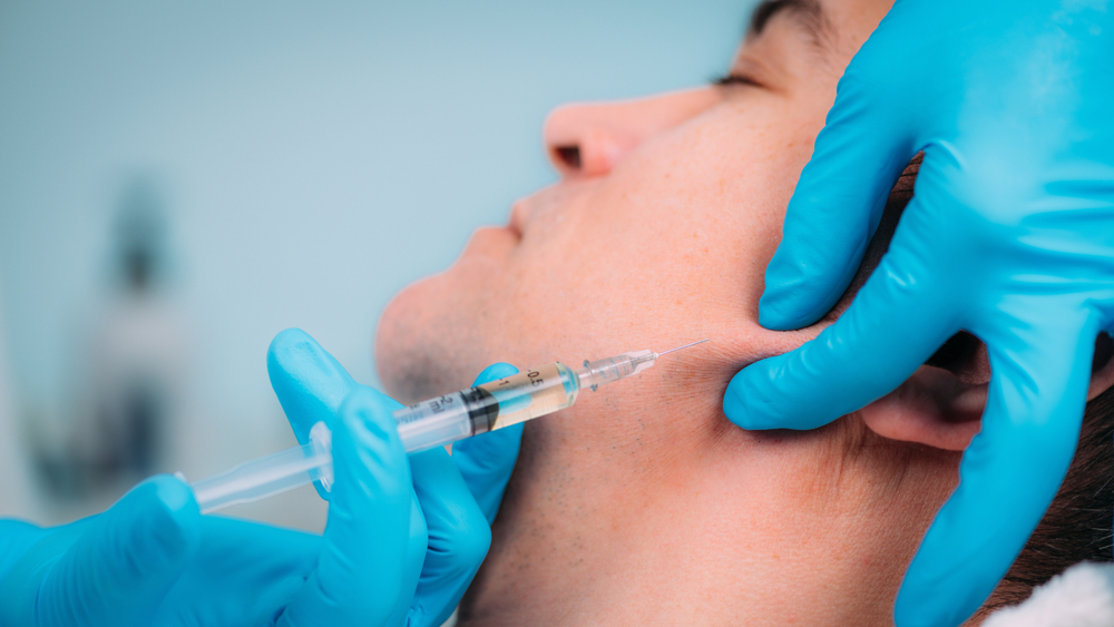 A healthcare professional administering a facial injection to a male patient, showcasing a close-up view of the procedure with a syringe and gloved hands.