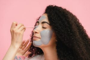 Womans hand painting her friends nose with gray clay mask