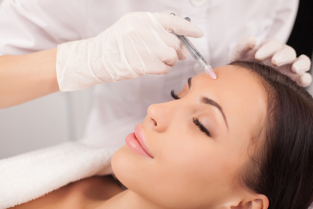 Aesthetic treatment session showing a dermatologist administering an injectable procedure on a woman's forehead, focusing on skin rejuvenation and wrinkle reduction.